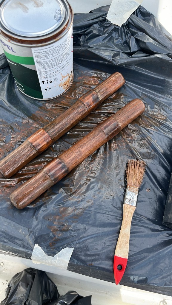 Hempel Teak Colour Restorer purk, pintsel ja kaks märga puitosa kile peal tekil